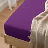 A close-up shot of a purple fitted sheet on a wooden bed frame, with a beige blanket draped over the corner. Produktbild-Vorschau