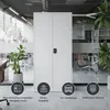 A white metal cabinet is shown in a modern office or workshop setting, with plants and office chairs visible in the background. Icons and text at the bottom suggest various uses for the cabinet. Náhľad obrázku produktu
