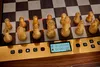 A close-up view of a wooden chess set on a digital chessboard with illuminated squares and a digital display showing game time. Podgląd zdjęcia produktu