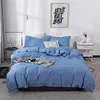 A neatly made bed with blue bedding, a decorative pillow, and a blanket draped over it, set in a bedroom with a framed picture on the wall.