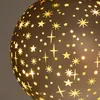 A close-up view of a decorative glass sphere with cut-out star patterns, illuminated from within. Náhled obrázku produktu