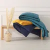 Three folded duvets in different colors are stacked on a wooden bench, with a decorative vase of dried grass to the left. Podgląd zdjęcia produktu