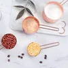 A set of rose gold measuring cups filled with different ingredients, arranged on a marble surface. Produktbild-Vorschau