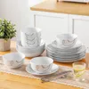 A set of white porcelain dishes with a black swirl pattern is arranged on a wooden table with a plant in the background. Náhled obrázku produktu