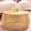 A gold coffee table with a decorative base, topped with a vase of flowers and a candle. Produktbild-Vorschau