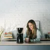 A woman is sitting at a kitchen counter with a coffee maker and a mug. Anteprima dell’immagine prodotto
