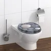 A toilet seat with a stone pattern is shown on a white toilet. A toilet brush holder is to the left, and a toilet paper holder is to the right. Anteprima dell’immagine prodotto