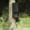 A black feeder is attached to a tree in a grassy, wooded area. Anteprima dell’immagine prodotto