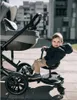 A baby sits on a stroller attachment while a stroller is beside them. Náhľad obrázku produktu