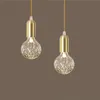 Two pendant lights with clear, patterned glass bulbs and gold fixtures hang against a brown background. Produktbild-Vorschau