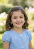 A young girl smiles at the camera, wearing blue earrings and a blue dress with white star patterns. Produktbild-Vorschau