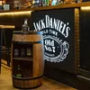 A wooden barrel-shaped bar with bottles of Jack Daniel's whiskey displayed inside and on top, set against a bar background with a Jack Daniel's logo. Náhled obrázku produktu
