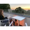A woman is reading a book on a balcony at sunset, with a patio heater warming the area. Podgląd zdjęcia produktu