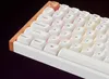A close-up, angled view of a white mechanical keyboard with a wooden trim and illuminated keys. Anteprima dell’immagine prodotto