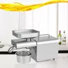 A stainless steel oil press machine is shown on a kitchen counter with bottles of liquid in the background. Náhled obrázku produktu