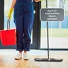 A person in blue overalls and yellow gloves is holding a red bucket and standing next to a mop on a wooden floor. Produktbild-Vorschau