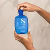 Hands holding a blue bottle of shampoo against a marble-like background. Anteprima dell’immagine prodotto
