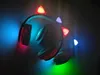 Several pairs of headphones with cat-ear shaped LED lights are displayed in a dark setting, illuminated by colorful lights. Náhled obrázku produktu