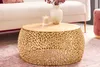 A gold metal coffee table with a filigree design, placed in a living room setting with a sofa and rug. Produktbild-Vorschau