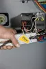 A person's hand is using a wire stripper tool on electrical wires inside a control panel. Anteprima dell’immagine prodotto