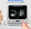 A mini dishwasher is shown on a white countertop, with kitchen utensils and a cup in the background. A hand is shown pressing a button on the dishwasher's control panel. Produktbild-Vorschau