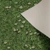 A close-up view of a green carpet with a pattern of daisies and clover, with a white sheet of paper partially covering the right side. Produktbild-Vorschau