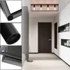 A hallway with a dark wooden door and white walls, featuring a black rectangular ceiling light with four exposed bulbs. Voir les images du produit
