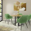 A dining set with green velvet chairs around a wooden table, with abstract art on the wall and natural light coming from a window. Náhled obrázku produktu