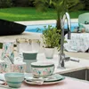 An outdoor setting with a pool and greenery, featuring tableware laid out on a counter with a faucet. Produktbild-Vorschau