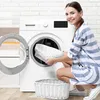A woman is putting a white bath mat into a washing machine. Voir les images du produit