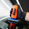 A gloved hand is holding a product and applying it to a dark surface. Produktbild-Vorschau