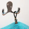A close-up of a towel clip attached to a hook on a white wall. Produktbild-Vorschau