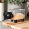 A clear plastic container shaped like an elephant, filled with toothpicks, sits on a wooden cutting board next to a plant and a bottle of olive oil. Náhľad obrázku produktu