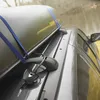 A close-up shot of a dark gray car roof with a dark green cargo box secured by blue straps and a black lock. Podgląd zdjęcia produktu
