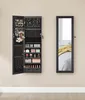 A wall-mounted jewelry cabinet with its door open, displaying various jewelry and cosmetics, next to a full-length mirror. Produktbild-Vorschau