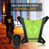 A person riding a bicycle at night, wearing a neon green LED signal vest. A remote control is in the foreground. Náhľad obrázku produktu