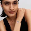 A woman wearing a black tank top, with her arm resting on her shoulder, showcasing a bracelet with a heart-shaped charm. Podgląd zdjęcia produktu
