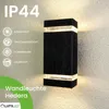 A black rectangular outdoor wall light with clear glass panels at the top and bottom, mounted on a textured wall. The image includes text and icons highlighting product features. Anteprima dell’immagine prodotto