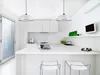 A modern, minimalist white kitchen with a large island, pendant lights, and a wall-mounted TV. Produktbild-Vorschau