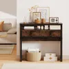 A small desk with drawers and decorative items on top, placed in a room with a sofa and rug. Náhled obrázku produktu