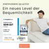 A man sitting on a sofa with cushions, with marketing text and certifications displayed. Produktbild-Vorschau