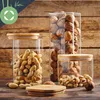 Three glass jars filled with nuts and peanuts, placed on a wooden surface. Produktbild-Vorschau