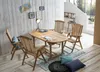 A wooden dining set with chairs and a table is arranged on a rug in a bright, airy room with wooden floors and a white paneled wall. Produktbild-Vorschau