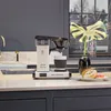 A Moccacoffee maker is shown on a kitchen counter with donuts and a plant in the background. Produktbild-Vorschau