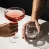 Two hands are holding glasses, one with pink liquid and the other empty. Produktbild-Vorschau