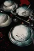 A table setting with plates, bowls, and wine glasses on a black tablecloth, decorated with red berries. Voir les images du produit