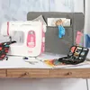 A white and pink sewing machine with a grey cover and various sewing accessories on a wooden desk. Produktbild-Vorschau
