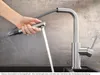 A hand is holding a pull-out spray head of a kitchen faucet, with water running from it into a sink. Podgląd zdjęcia produktu