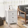 A white nightstand with three drawers is placed next to a gray armchair in a room with sheer curtains and wooden flooring. Podgląd zdjęcia produktu