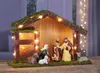 A nativity scene with figures and animals inside a wooden stable, decorated with moss and fairy lights. Produktbild-Vorschau